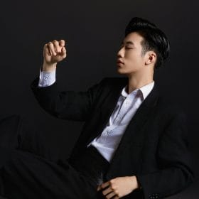 Profile of a young Vietnamese man in a stylish black suit posing in a studio.