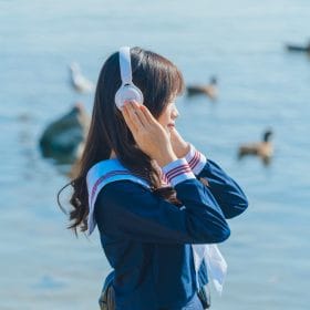 Teenage girl in sailor suit with headphones by a lake, serene and stylish.