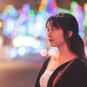 Profile of a woman with eyeglasses against colorful blurred city lights at night.